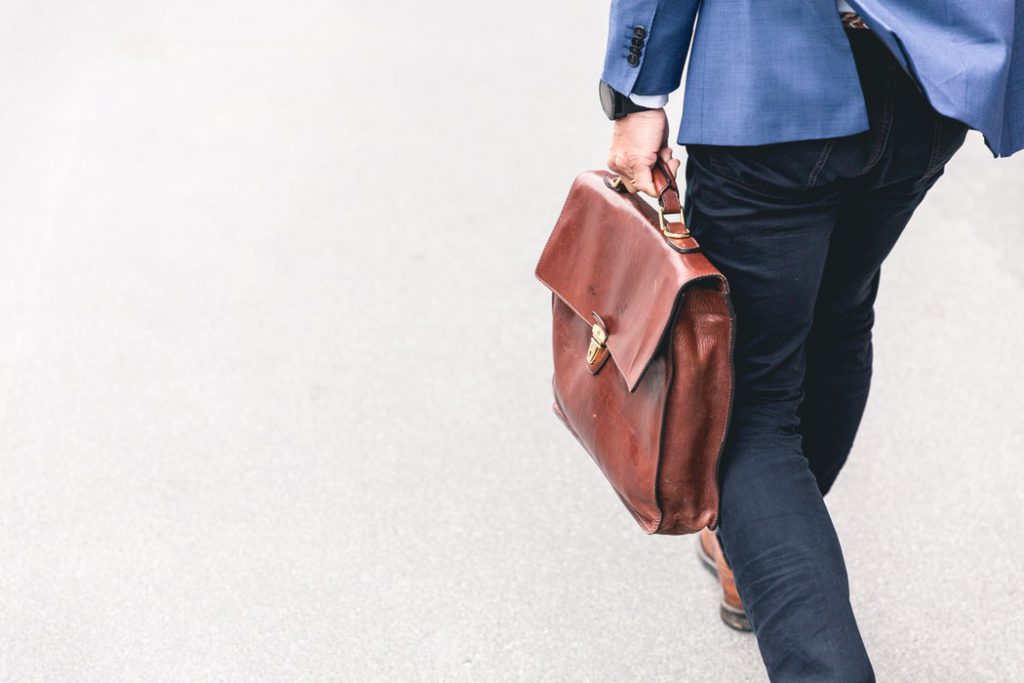 Man wearing business casual attire walking with briefcase on pavement