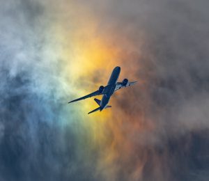 Plane flying in clouds the colour of rainbows.