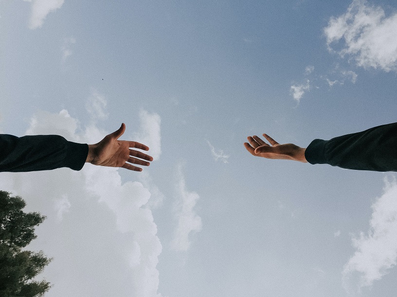 Two hands reaching across a blue sky with clouds