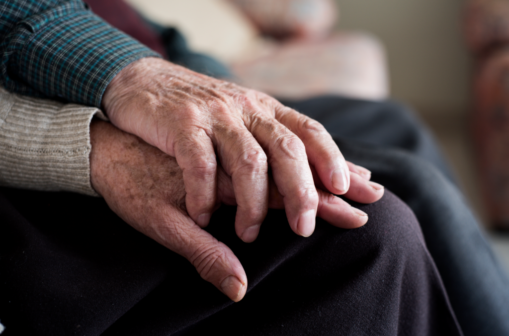 Two elderly hands resting on a thigh