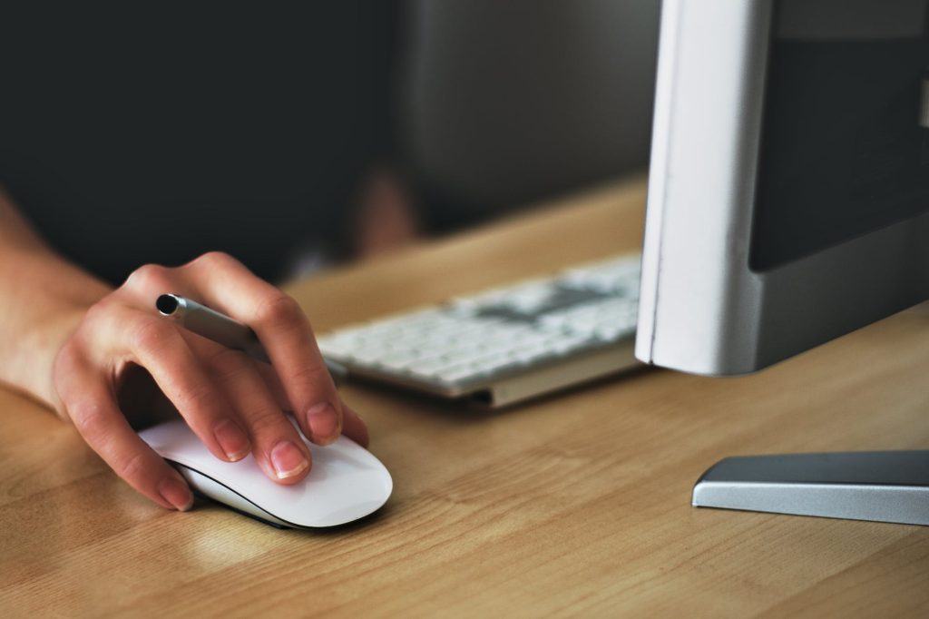 A hand on a mouse with a computer nearby