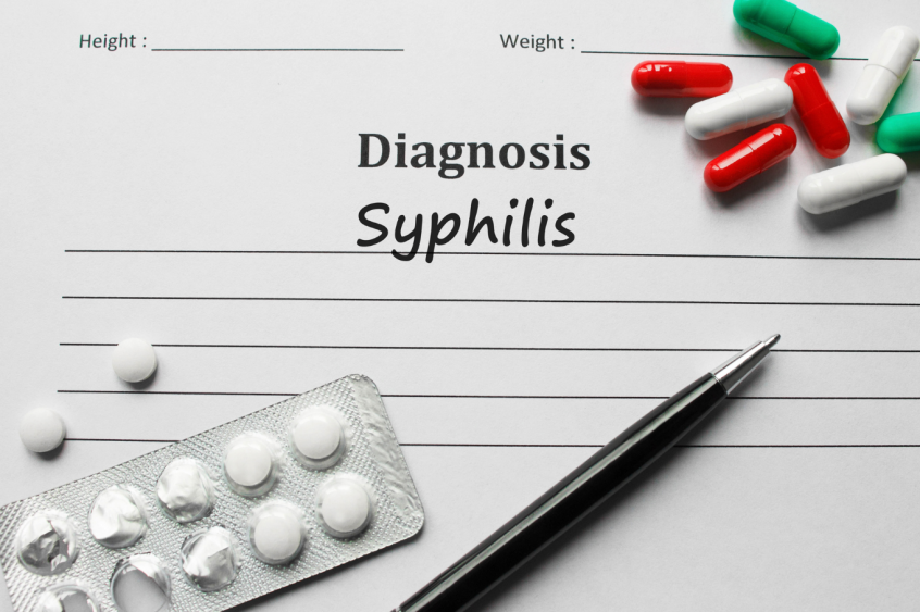 A doctor's notepad that says diagnosis syphillis with some coloured pills on the page