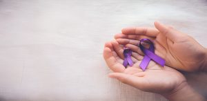 Two hands holding two purple awareness ribbons